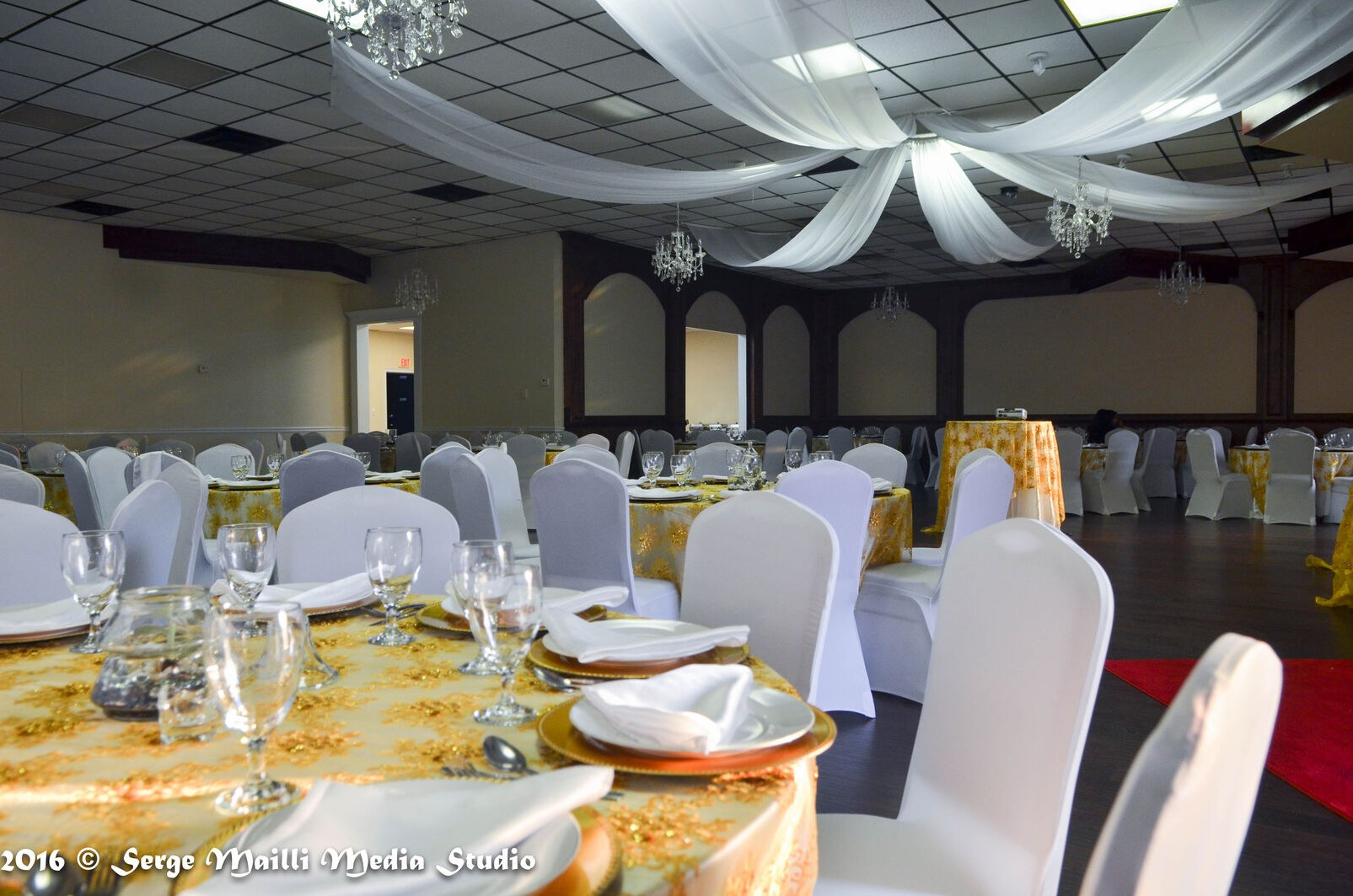 The completed graduation celebration room set with gold linens, white chair covers and draped ceiling