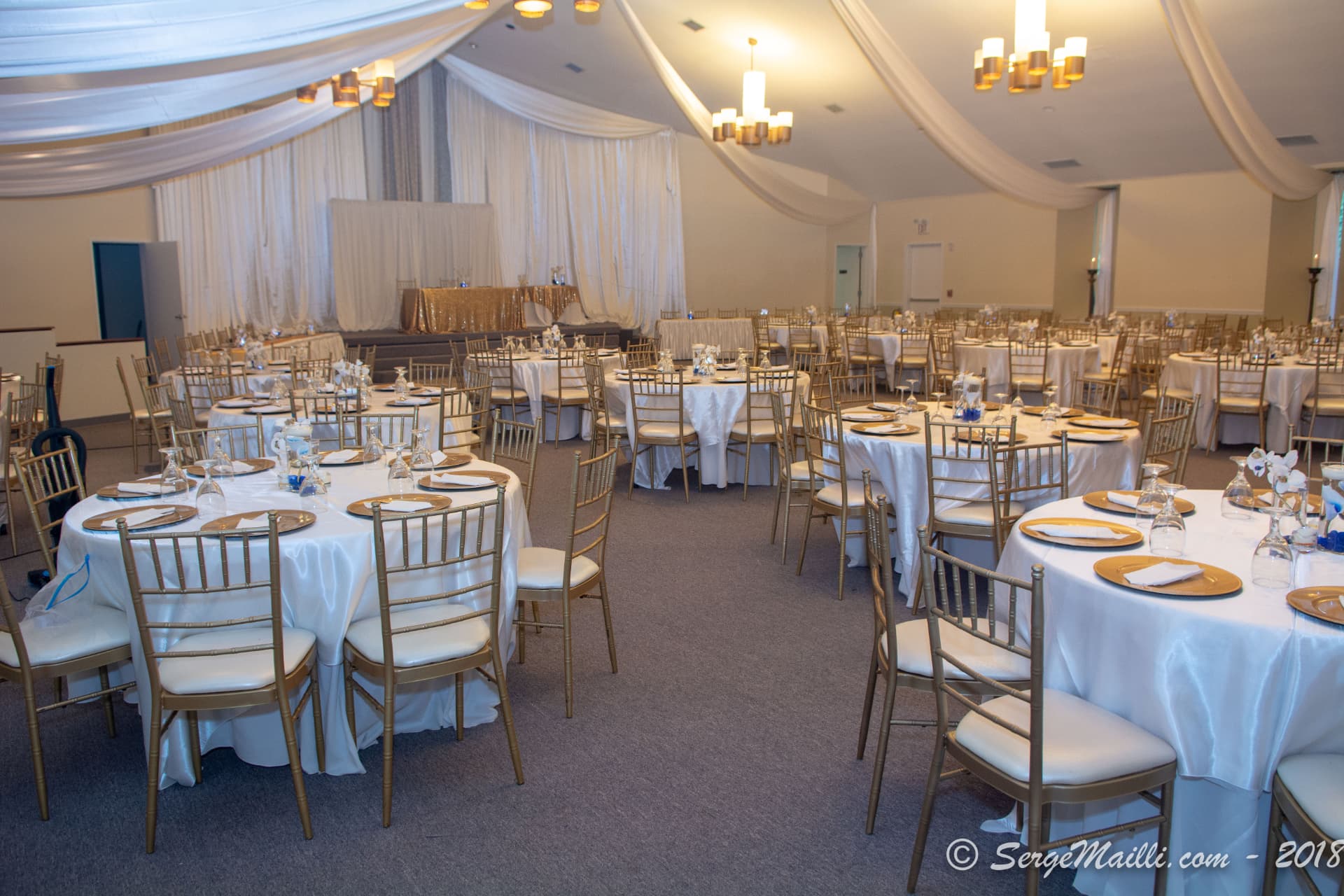 Reception hall prepared for the Marcelle and Miguel celebration with gold chiavari chairs and white linens
