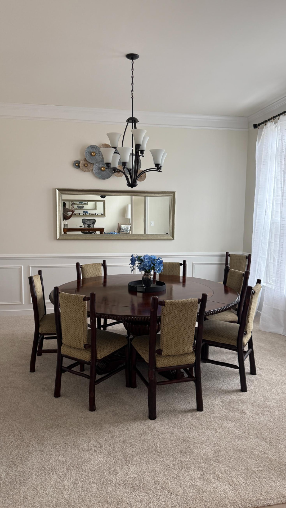Dining room with round table for eight, chandelier and framed mirror